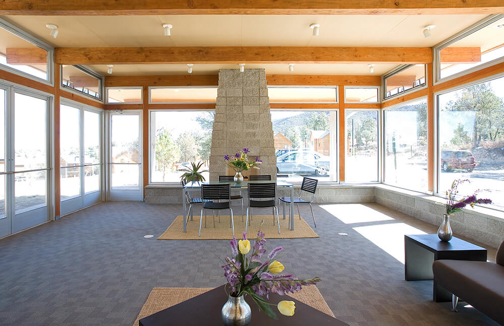 Sunlit community building at Ladera with glass walls, timber beams, and a stone fireplace